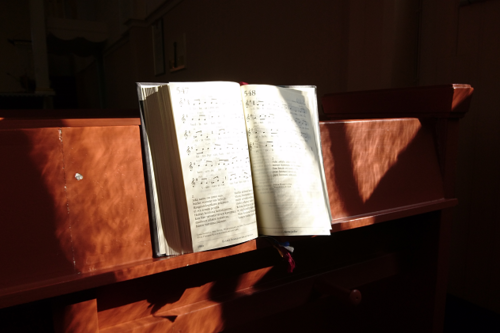 Virsikirja kirkonpenkissä, aurinko paistaa kirjan sivuille